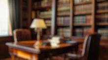 Blurred background of a beautifully designed law office featuring a classic wooden desk, comfortable chairs, and extensive bookshelves filled with law books, creating a warm and inviting workspace.